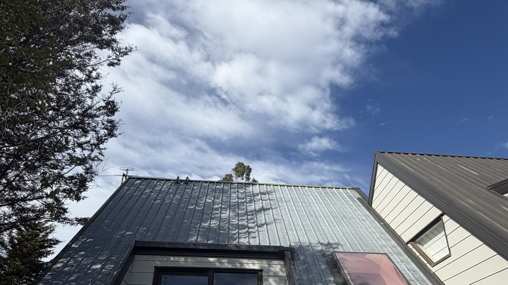 Faded, chalky grey long-run roof on a two storey Kaiapoi house before cleaning and painting