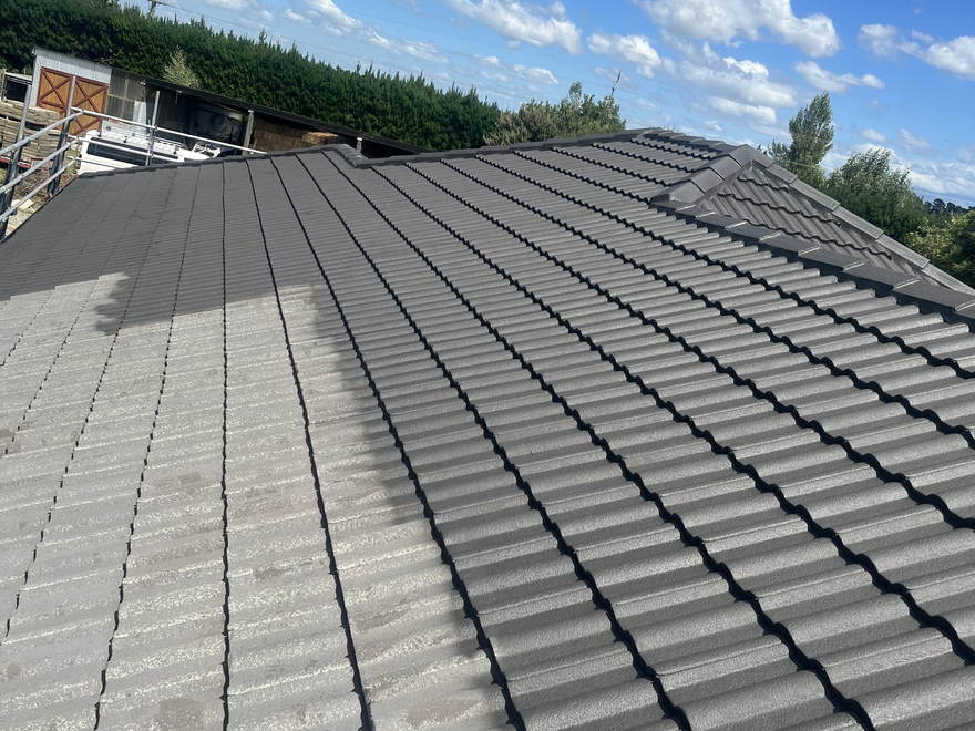 Concrete tile roof half painted, bare grey tiles on one side and new charcoal coating on the other