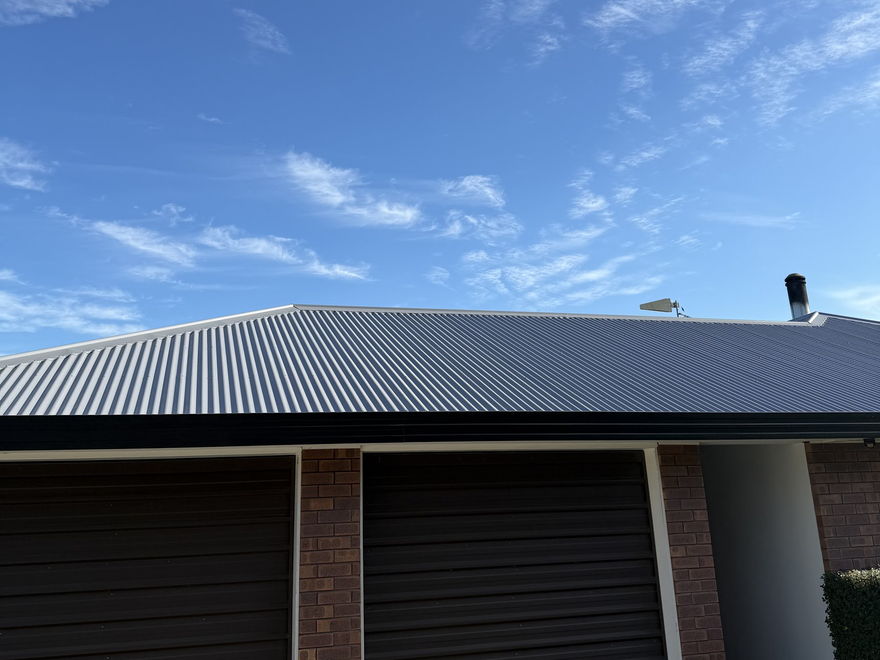 Corrugated iron hip roof painted light grey over a brick garage